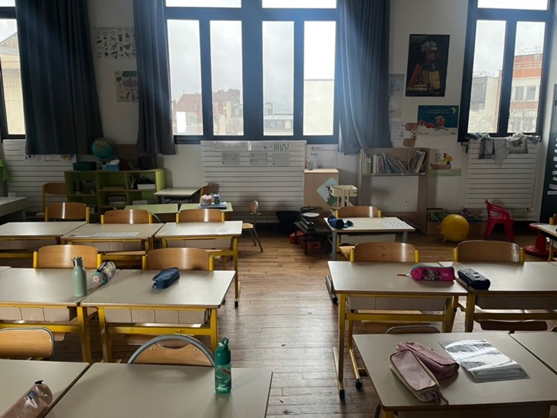 Salle de classe vide avec bureaux alignés et grandes fenêtres.