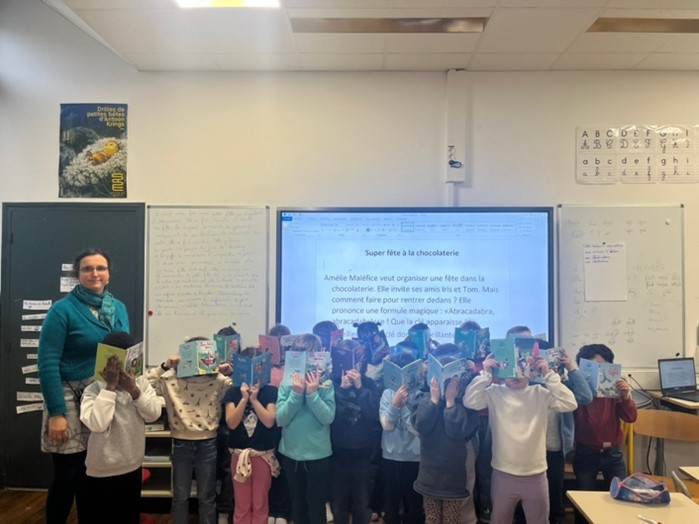 Classe d’élèves debout tenant des livres devant un tableau.