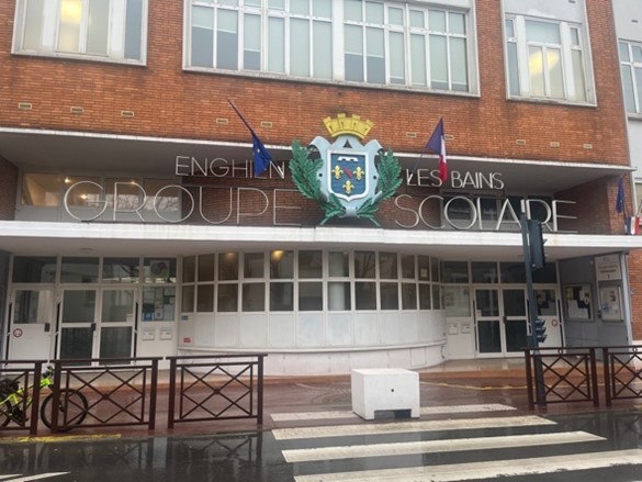 Entrée d’un groupe scolaire avec blason et drapeaux.